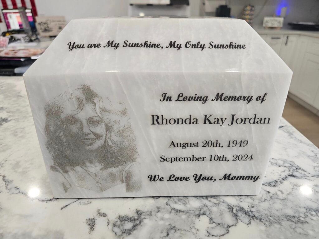 A Personalized White Marble Memorial Plaque Featuring An Engraved Portrait Of A Woman And An Inscription In Loving Memory Of Rhonda Kay Jordan, Including Her Birth And Death Dates.