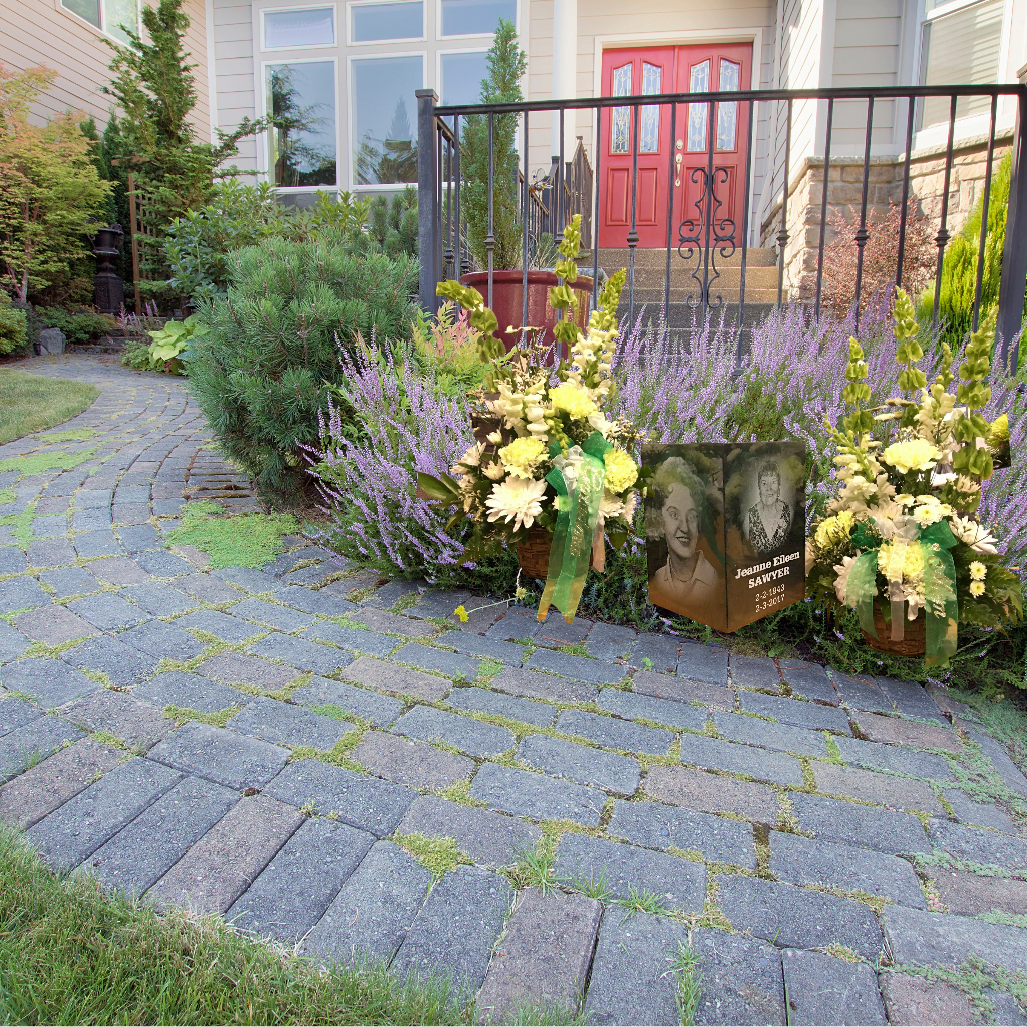 A Granite Memorial Urn With Engraved Portraits Placed In A Beautifully Landscaped Home Garden, Surrounded By Flowers.