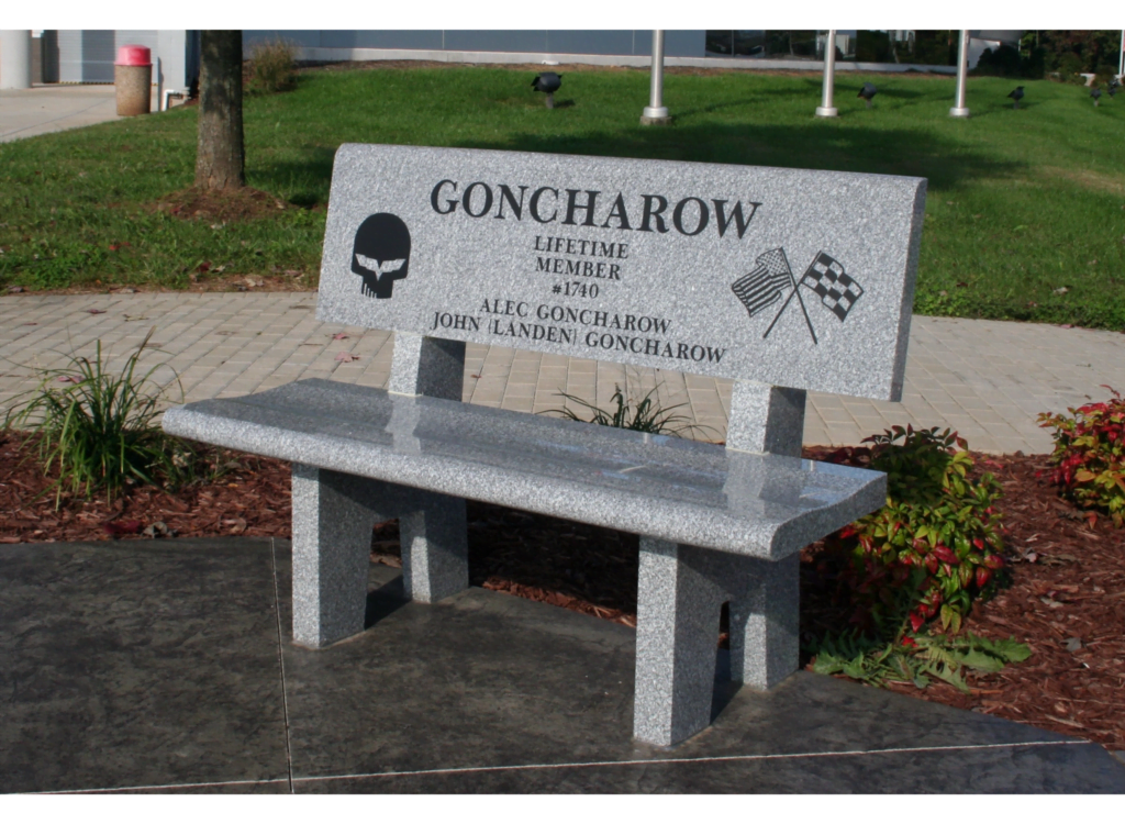 Granite Memorial Bench Engraved By Sandblasting With The Name &Quot;Goncharow,&Quot; Lifetime Member #1740, And Featuring Engraved Symbols Of A Skull And Crossed Racing Flags.