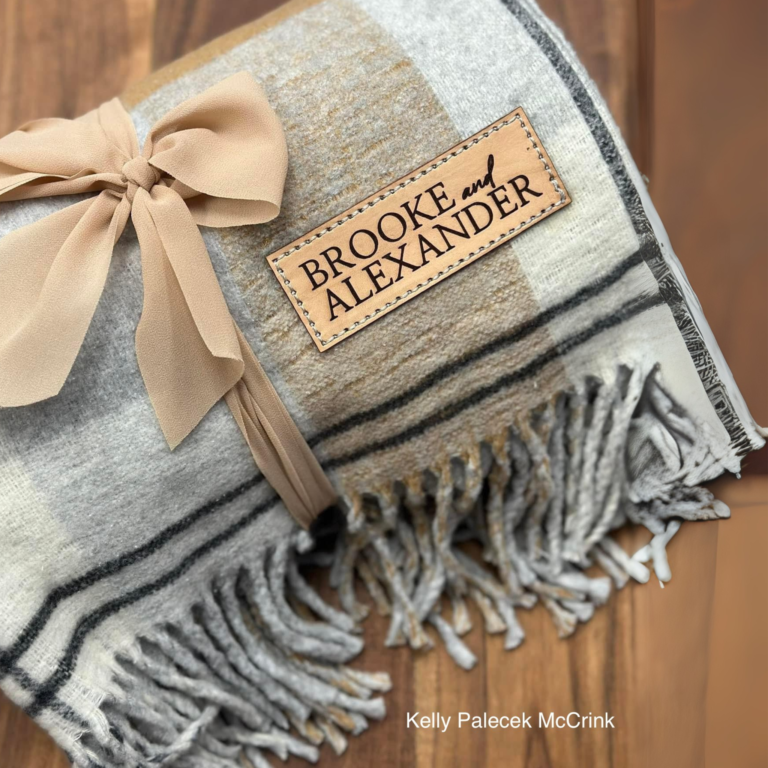 Cozy folded blanket with an AP Lazer engraved leather patch reading “Brooke and Alexander,” tied with a soft beige ribbon.