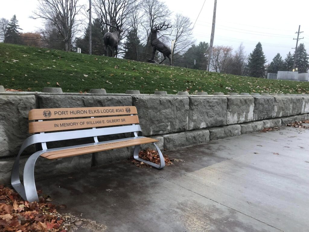 A memorial bench engraved by an AP Lazer machine sits in a public garden.